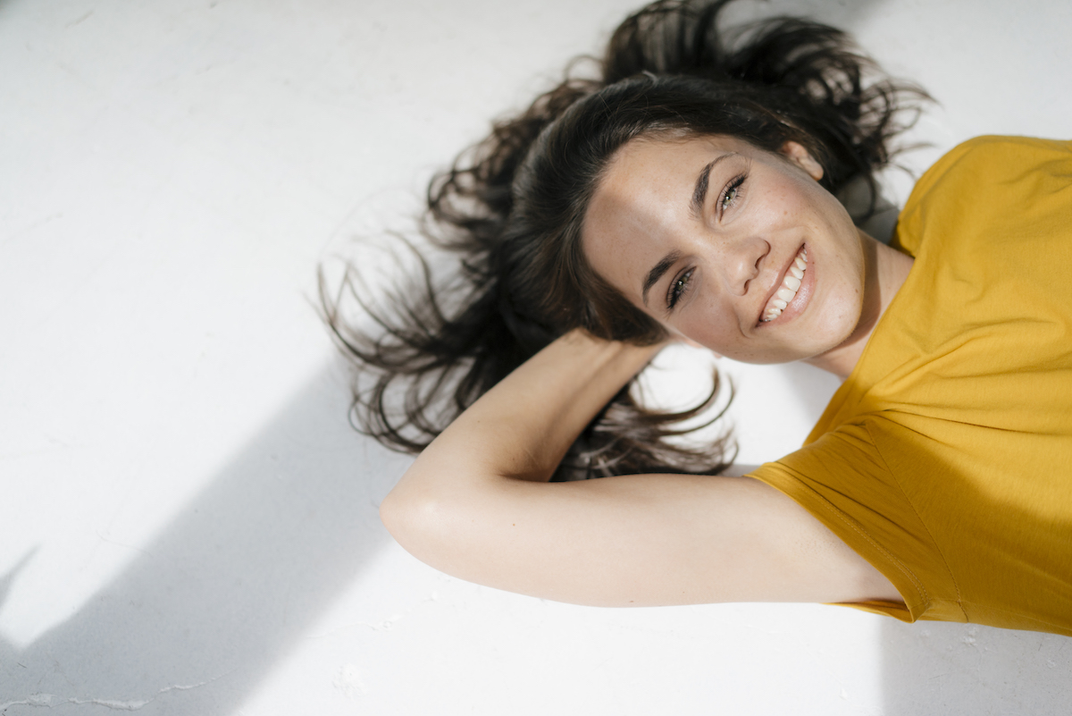 Brunette lying on the ground with her head supported by one hand, smiling