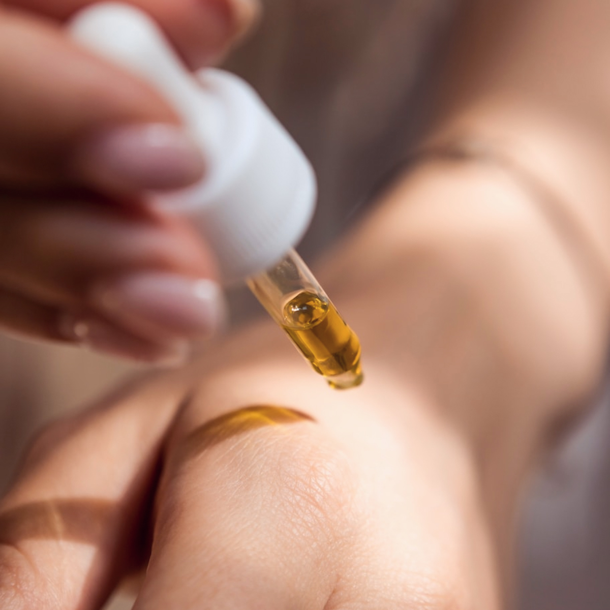 Close up of a pipette of golden liquid over someone's hand.