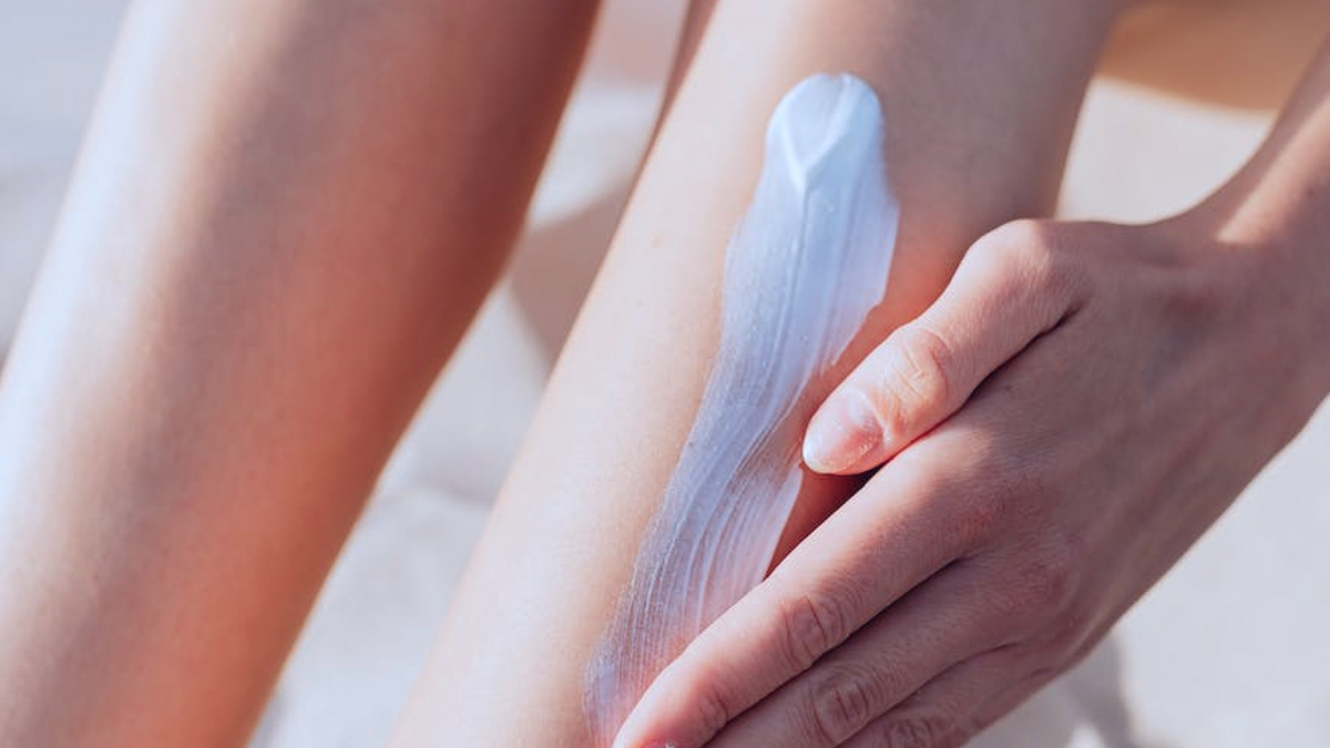 Close up of a hand applying white lotion to their calf.