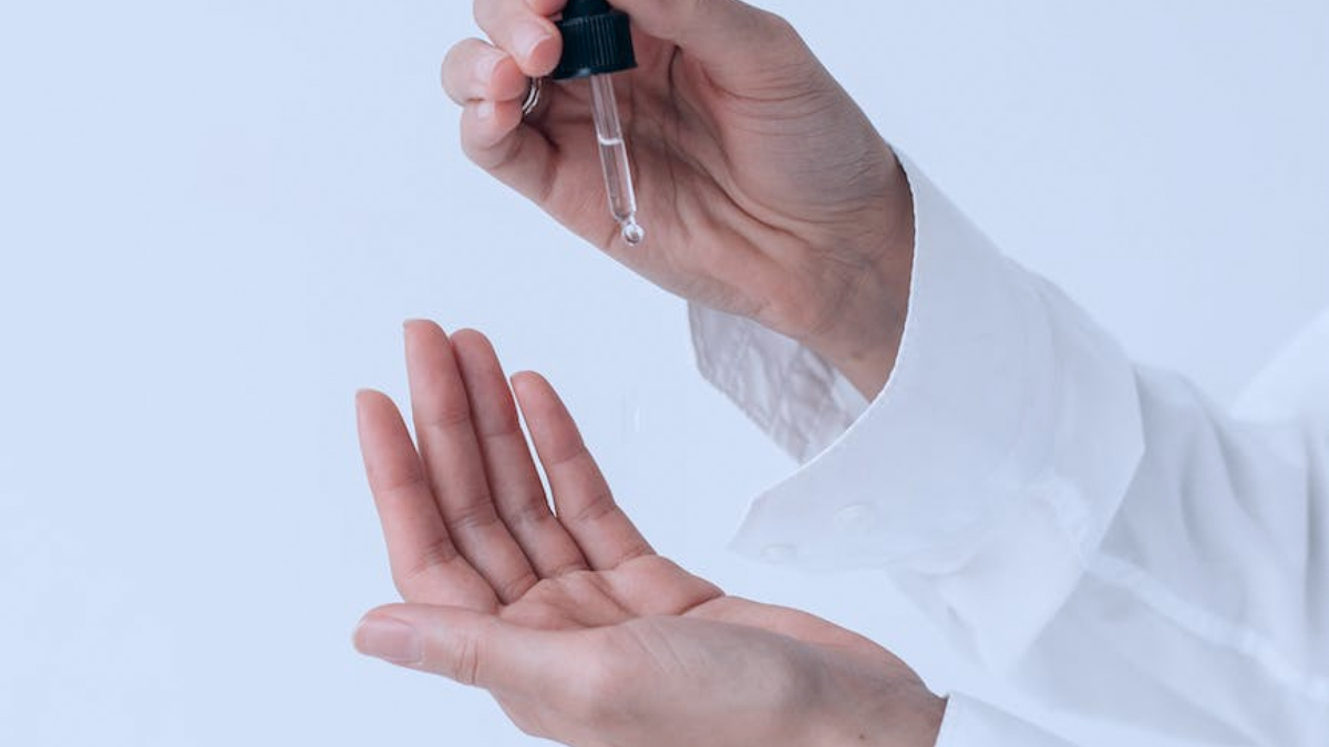 A person holds a pipette of clear liquid over their other empty hand.
