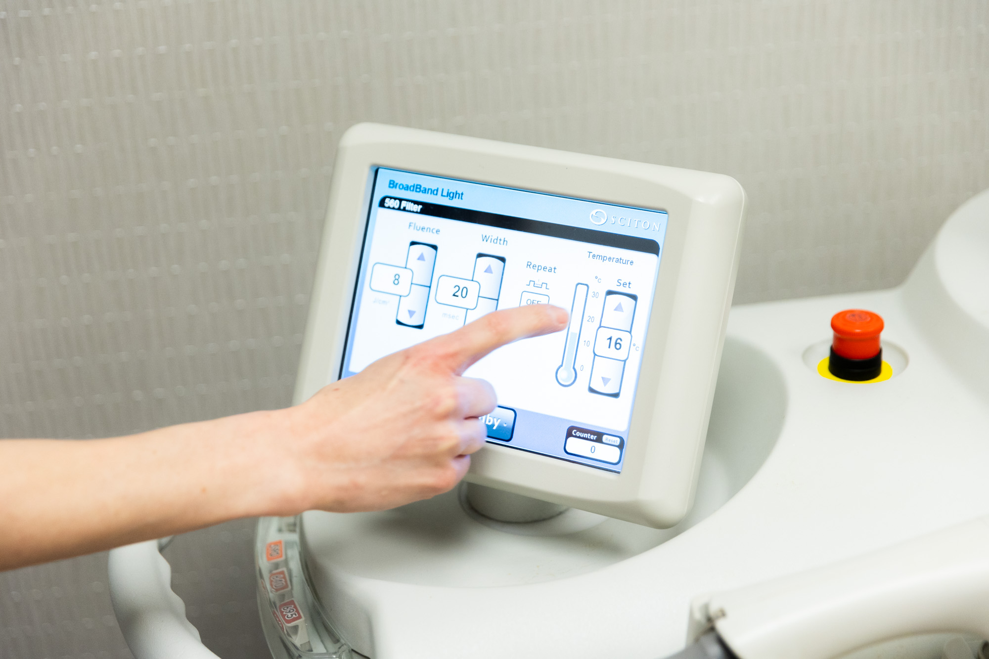 A hand gestures at one of the settings on a Sciton machine's screen. The temperature currently is set at 16.