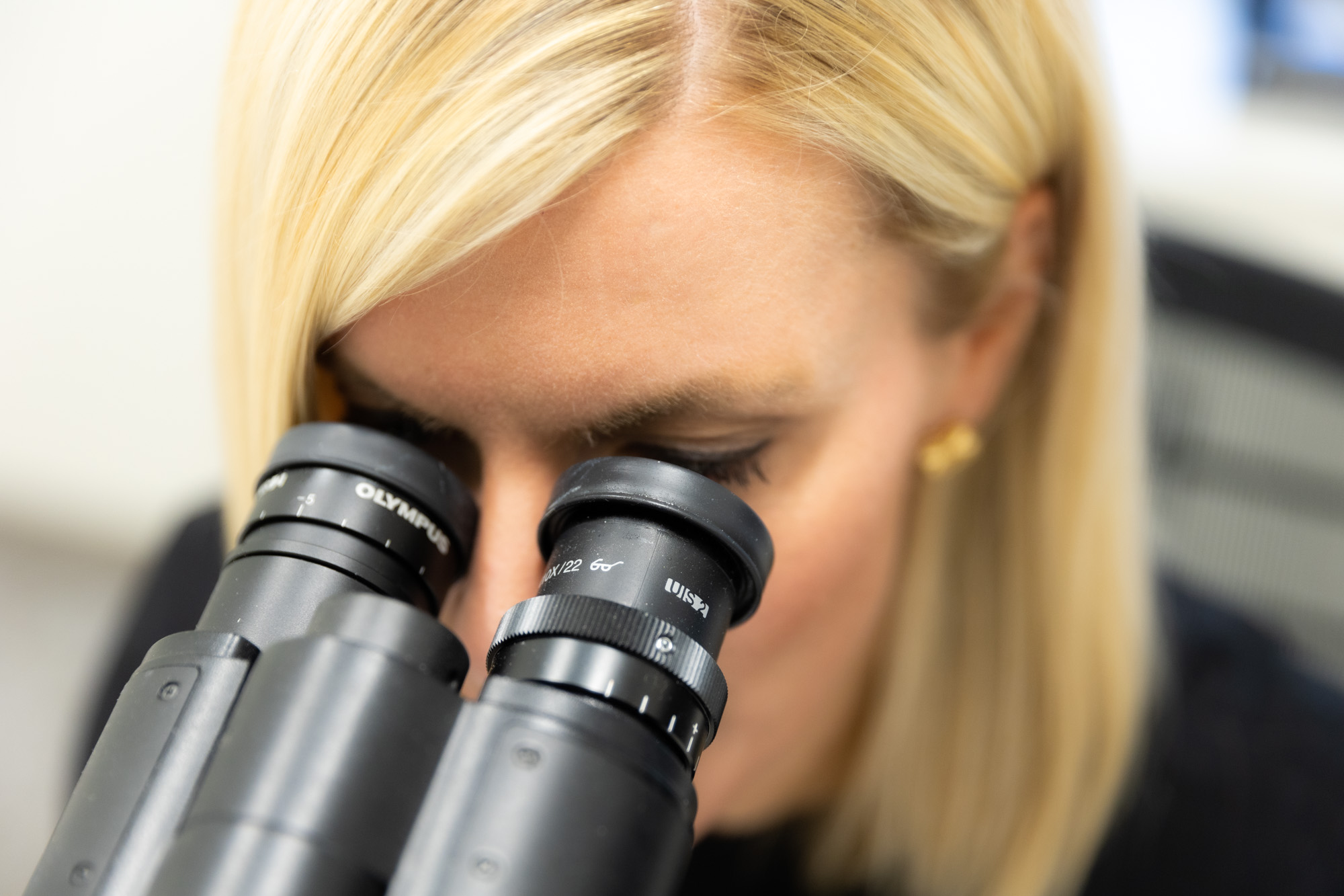 A female Kansas City Skin and Cancer Center provider looks into a microscope. Only her face and the top of the microscope is visible.