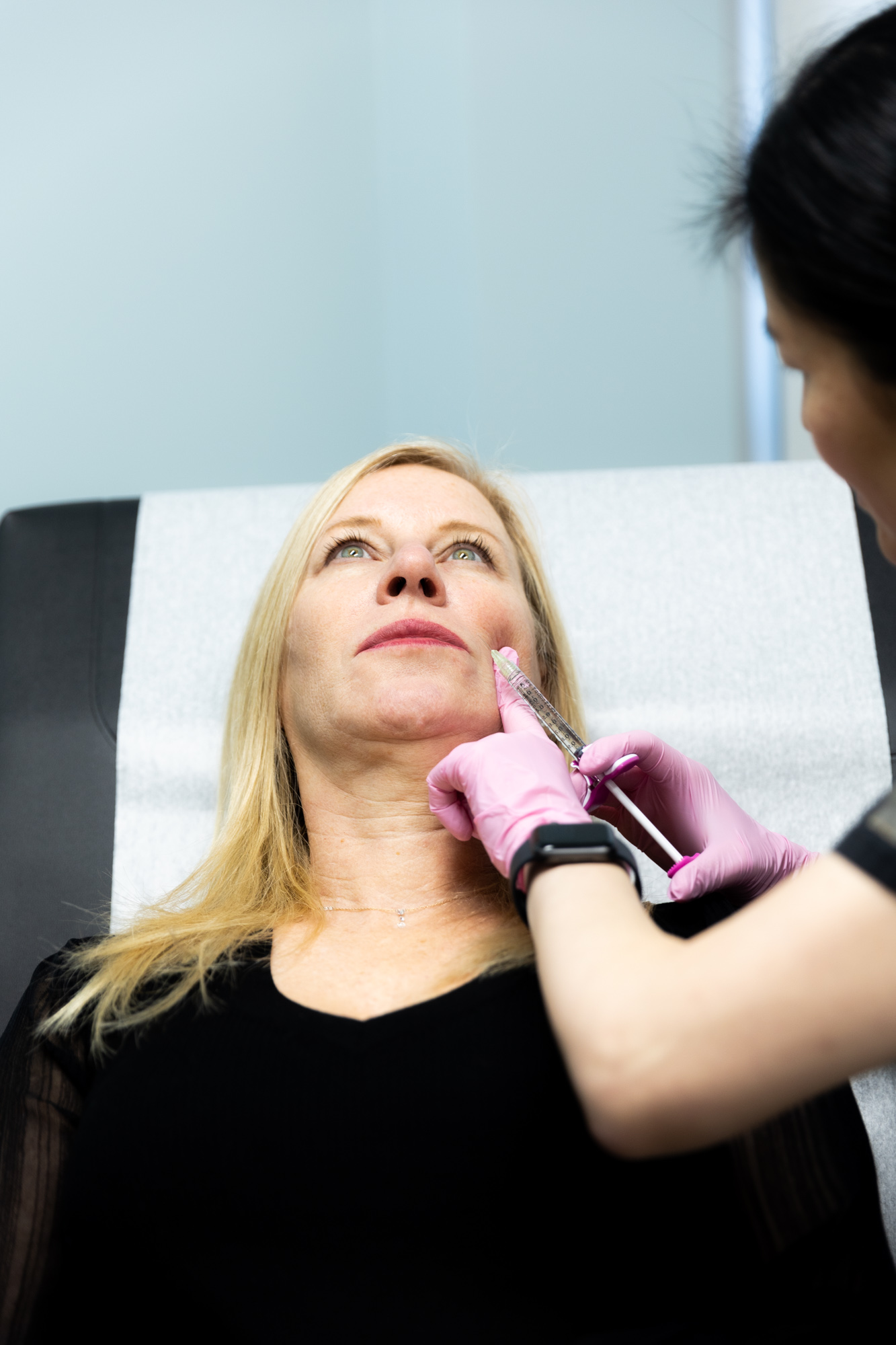 A Kansas City Skin and Cancer Center doctor begins to inject filler into a female patient's left cheek. Patient is reclining back and looking up.