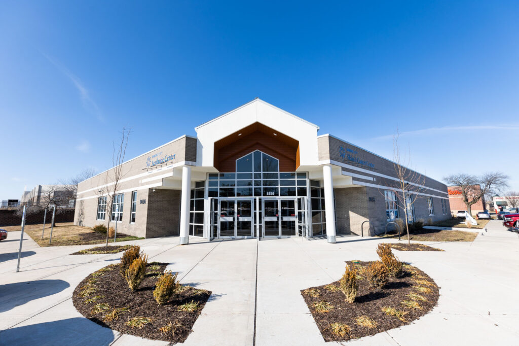 Image of the front of the building, where you can come for a Hyperpigmentation Treatment in Kansas City. It is mirrored on both sides. The entryway is made of glass windows, and the exterior that is visible is made of brick.