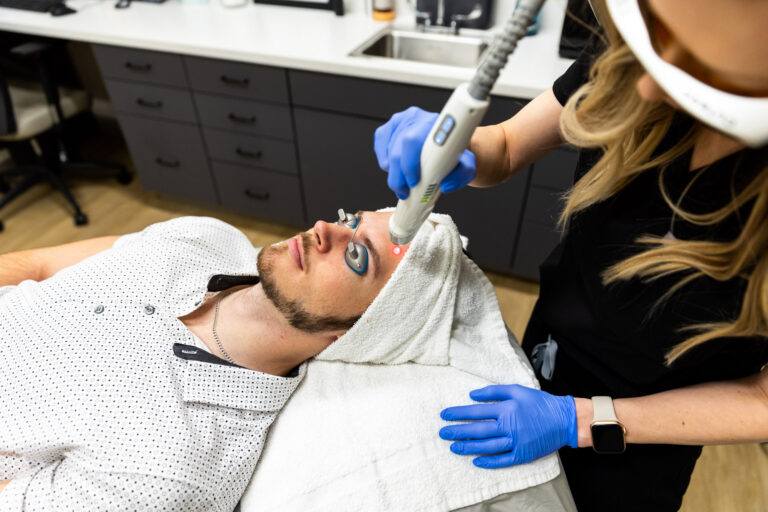 Patient at Kansas City Skin & Cancer Center receives a Laser Genesis treatment in Overland Park, KS. He is lying on his back wearing protective eyewear as his provider guides the handpiece over his forehead.