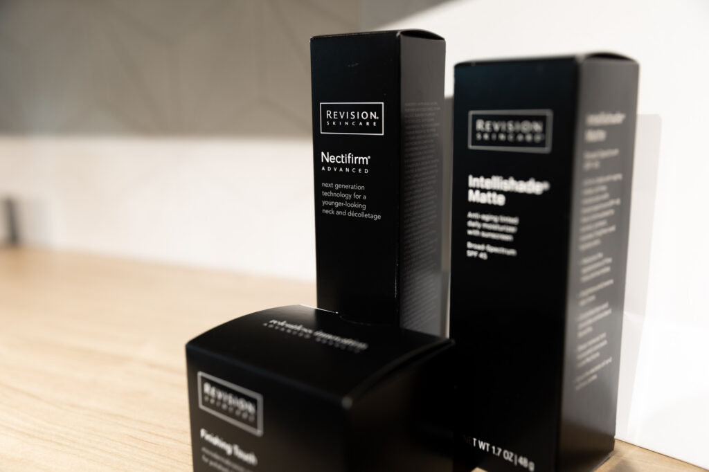A Kansas City Skin and Cancer Center professional is holding and gesturing at a box of skincare. A client stands out of focus towards the front of the image.