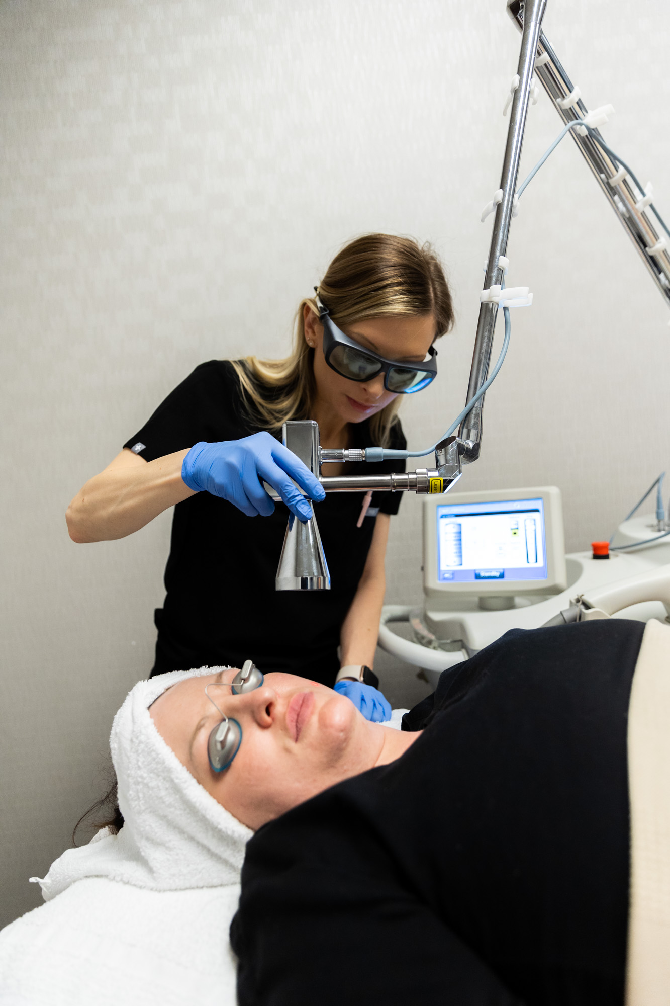 A female Kansas City Skin and Cancer Center provider uses the Micro Laser device to perform a Micro Laser Peel on a female client. Client is wearing protective eye coverings and has a towel covering her hair.