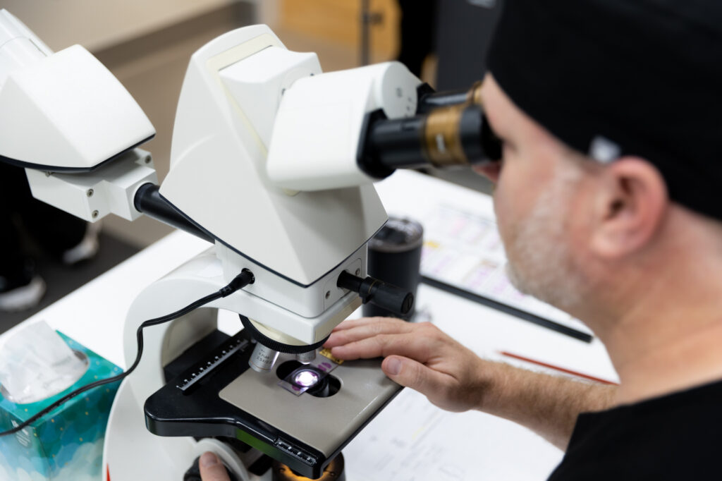 A Kansas City Skin and Cancer Center medical professional uses a microscope to examine a sample.