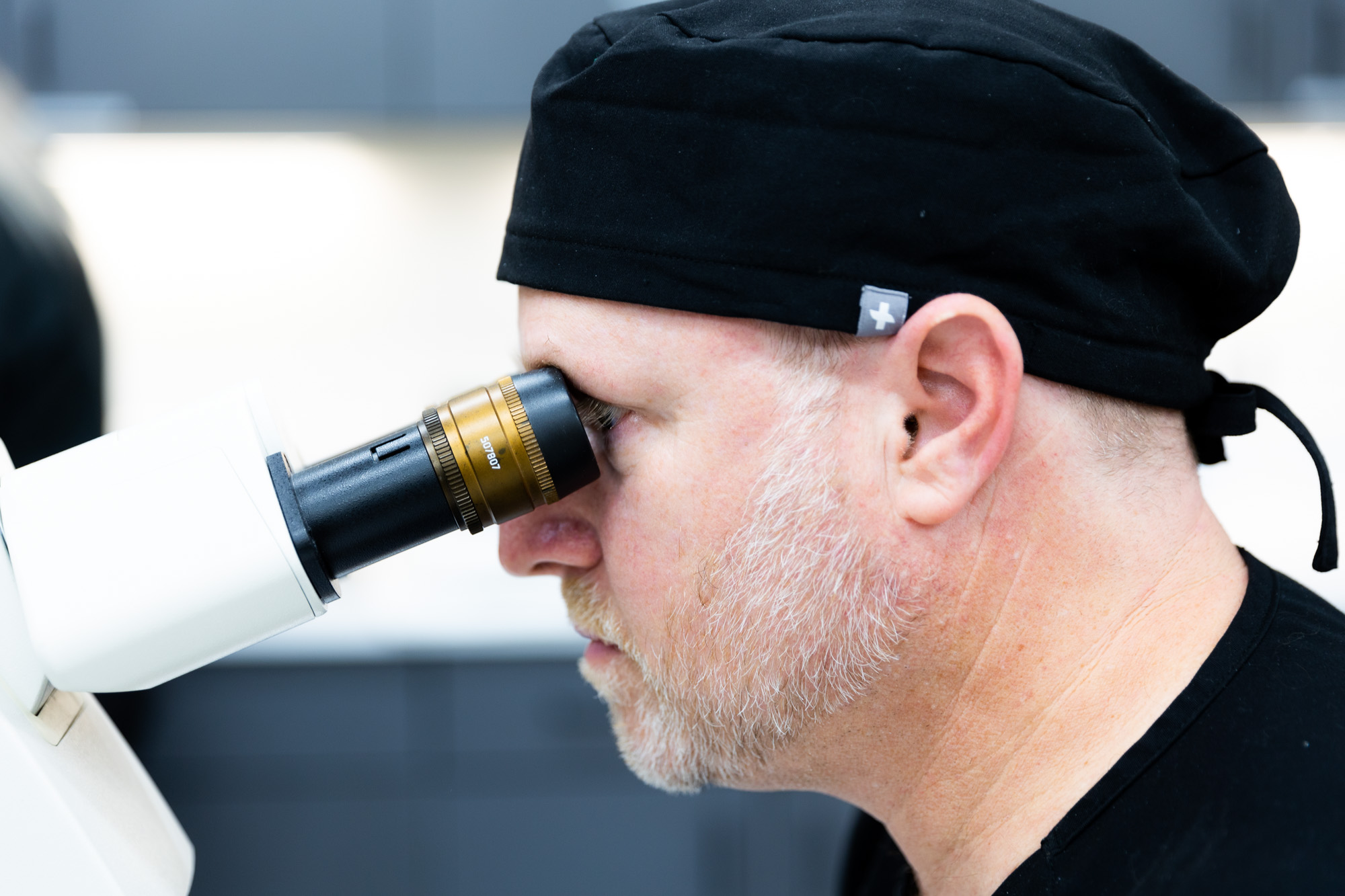 A Kansas City Skin and Cancer Center medical provider looks into a microscope in order to examine a sample. Only the provider's head and top of the microscope are visible.