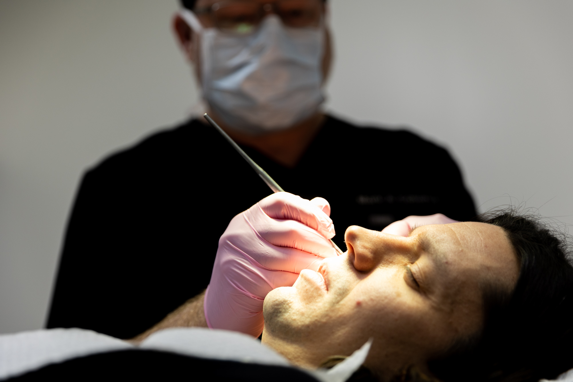 A male Kansas City Skin and Cancer Center provider performs a Mohs surgery on a paitent. Image is taken from the left side of the patient, so actual surgery is not visible as the doctor is workin on the right side of the face.