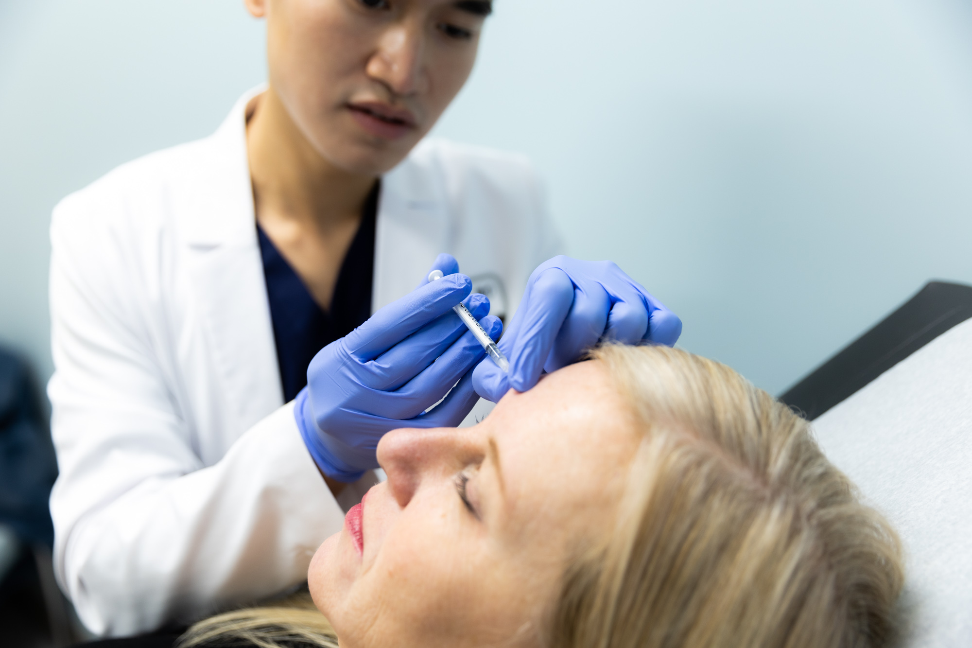 A Kansas City Skin and Cancer Center doctor administers an injectable treatment for female patient. He holds the shot up to her forehead, and her eyes are closed.