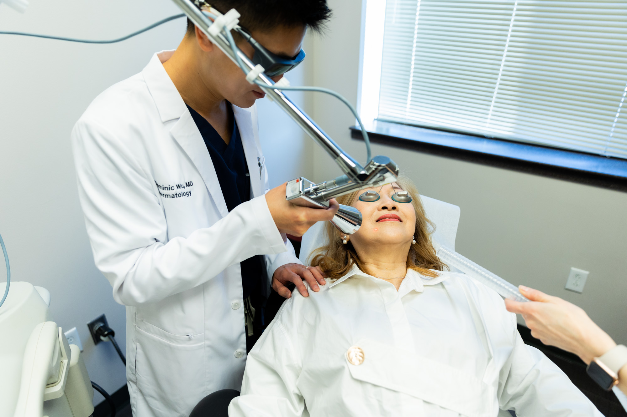 A Kansas City Skin and Cancer Center doctor holds the Contour TRL machine several inches away from a female client's face. The client is lying down with eye protection on.