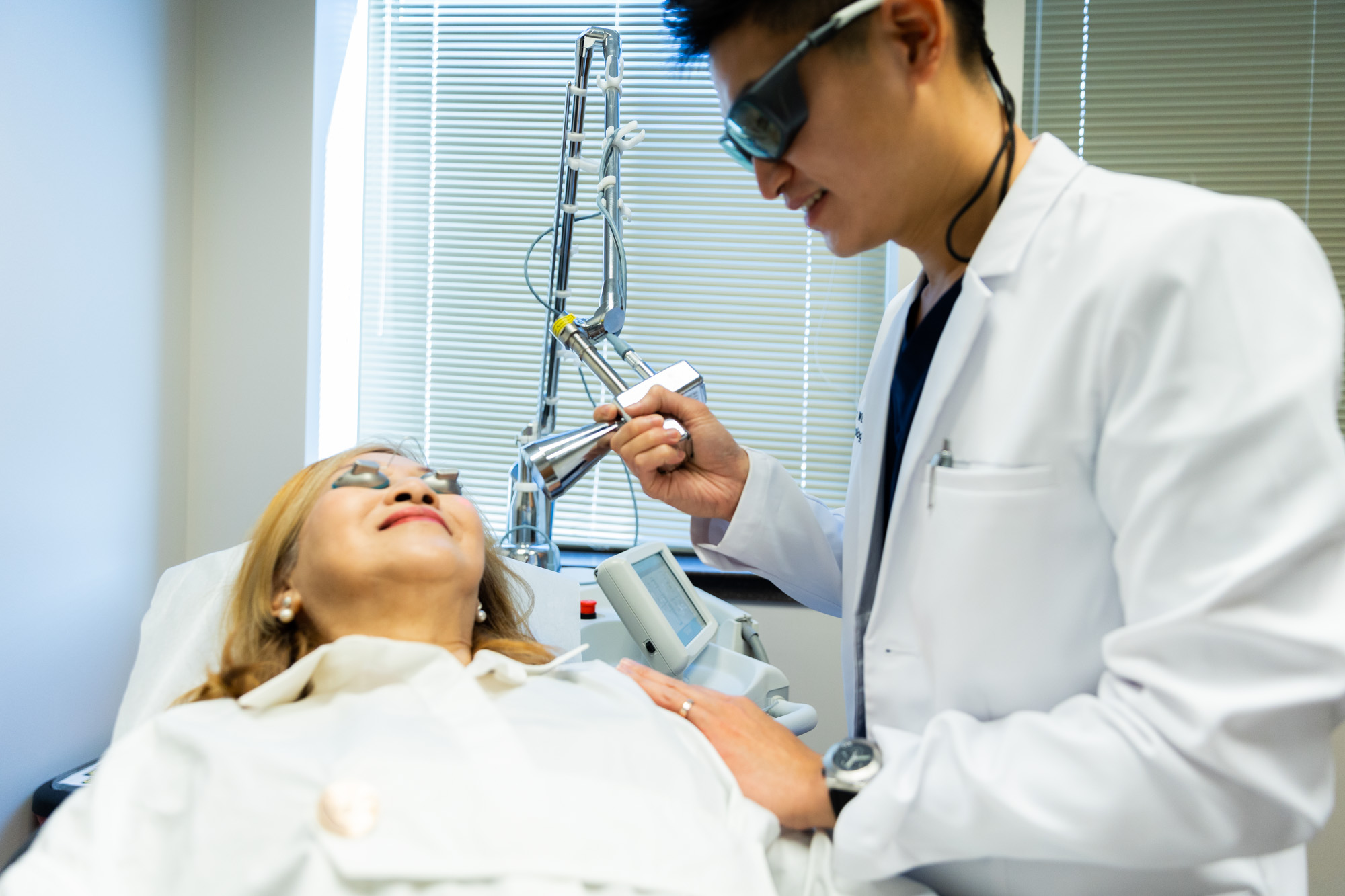 A Kansas City Skin and Cancer Center doctor holds the Contour TRL machine several inches away from a female client's face. She is lying down with eye covers on.