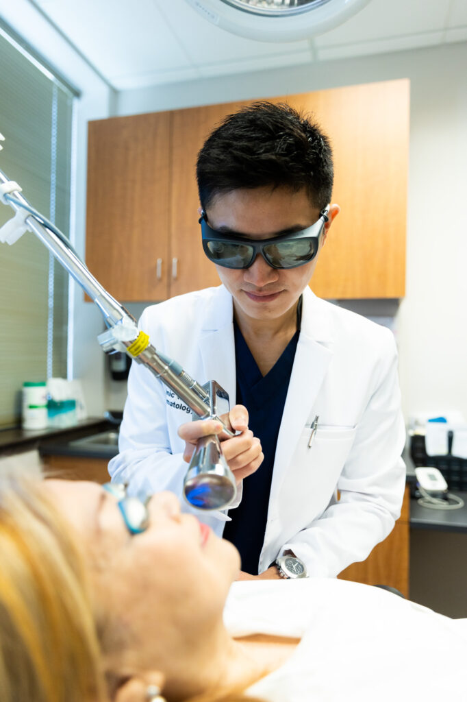 A Kansas City Skin and Cancer Center doctor holds the Contour TRL machine several inches away from a client's face. The client is lying down with protective eye covers. The doctor wears protective goggles.