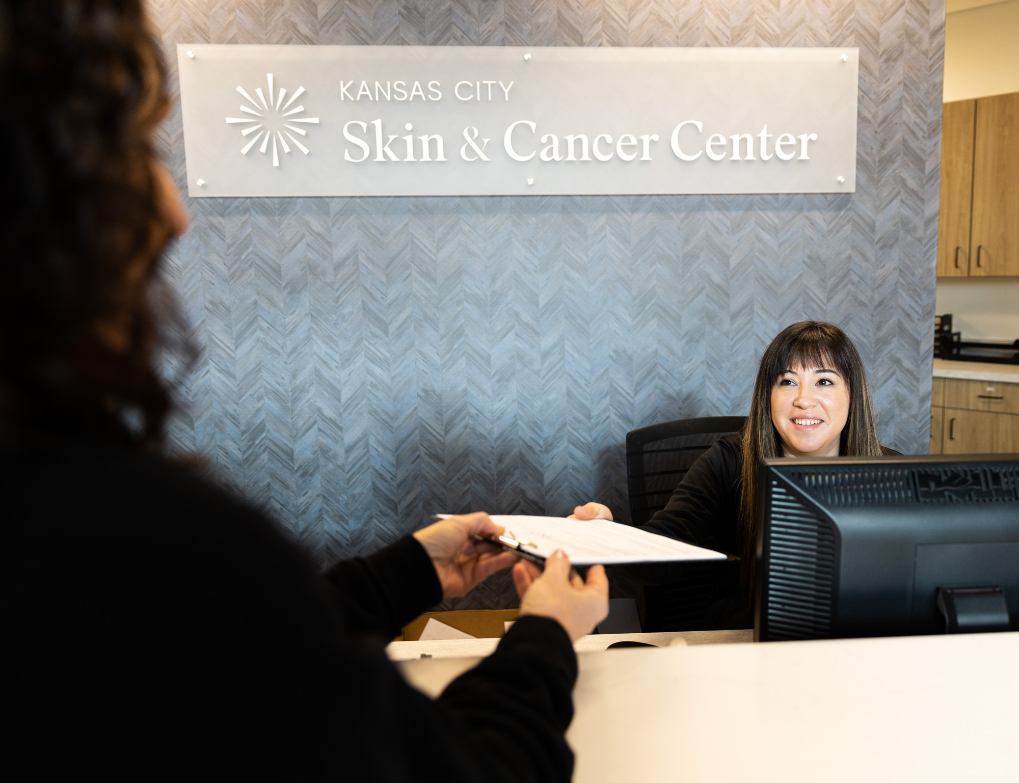 A female client takes a clipboard from the receptionist at Kansas City Skin and Cancer Center.