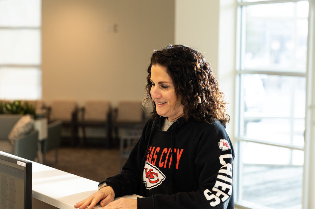 A female client smiles as she stands at the check in desk of Kansas City Skin and Cancer Center.