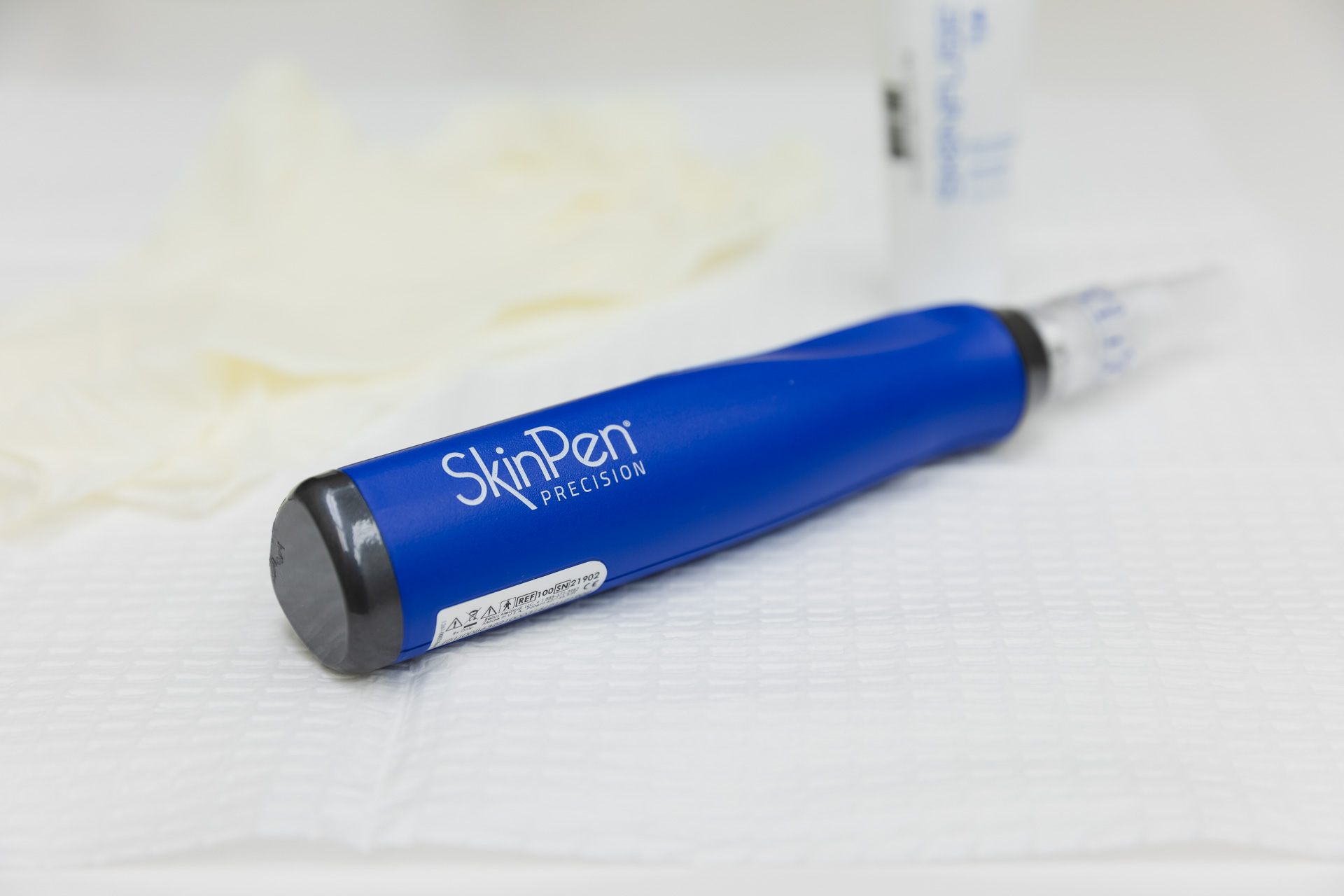 A female Kansas City Skin and Cancer Center professional uses a skin pen on a male client's forehead. The patient is lying down with a towel covering his hair.