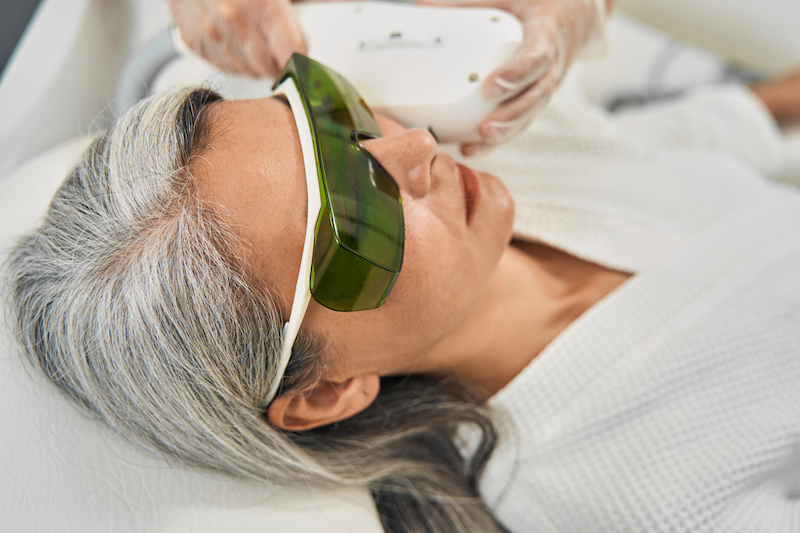 An older woman is lying down with protected glasses over her eyes for a session of intense pulsed light therapy in Kansas City.