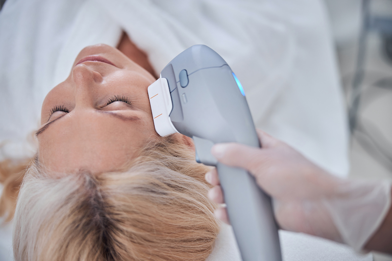 A woman is lying down and has the device for intense pulsed light in Kansas City pressed to her face for treatment.